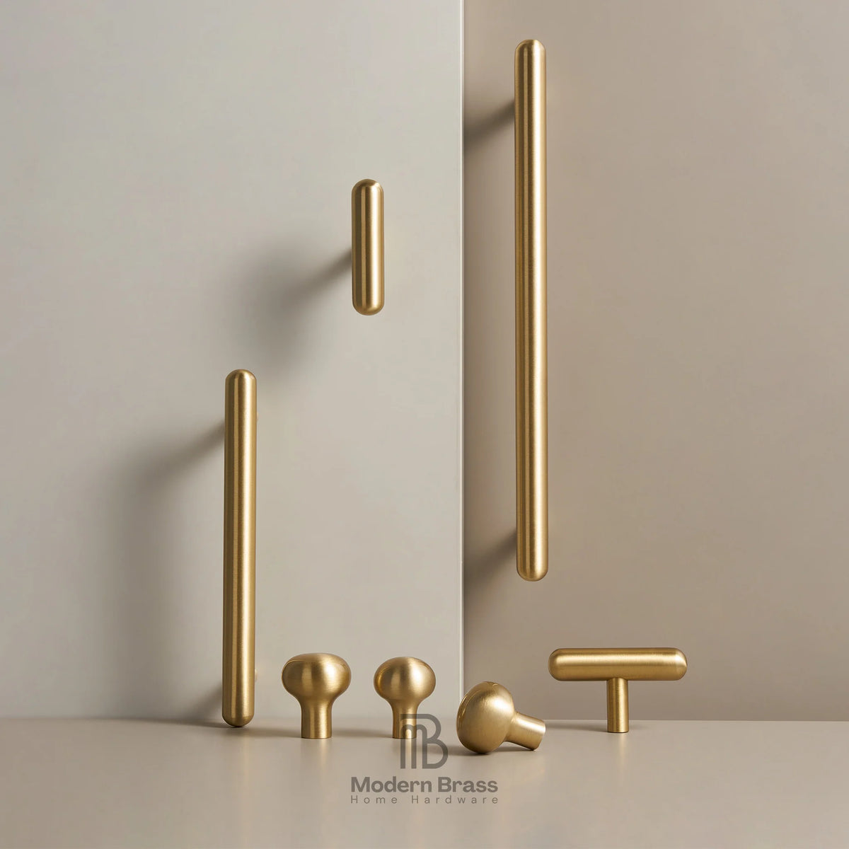 A set of modern brass cabinet knobs in various shapes and sizes, including long bar handles, round ball knobs, and T-bar handles, displayed on a light beige surface against a matching beige background.