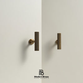 Two modern cylindrical cabinet handles in a textured bronze finish mounted on a minimalist off-white wall, with the Modern Brass logo at the bottom.