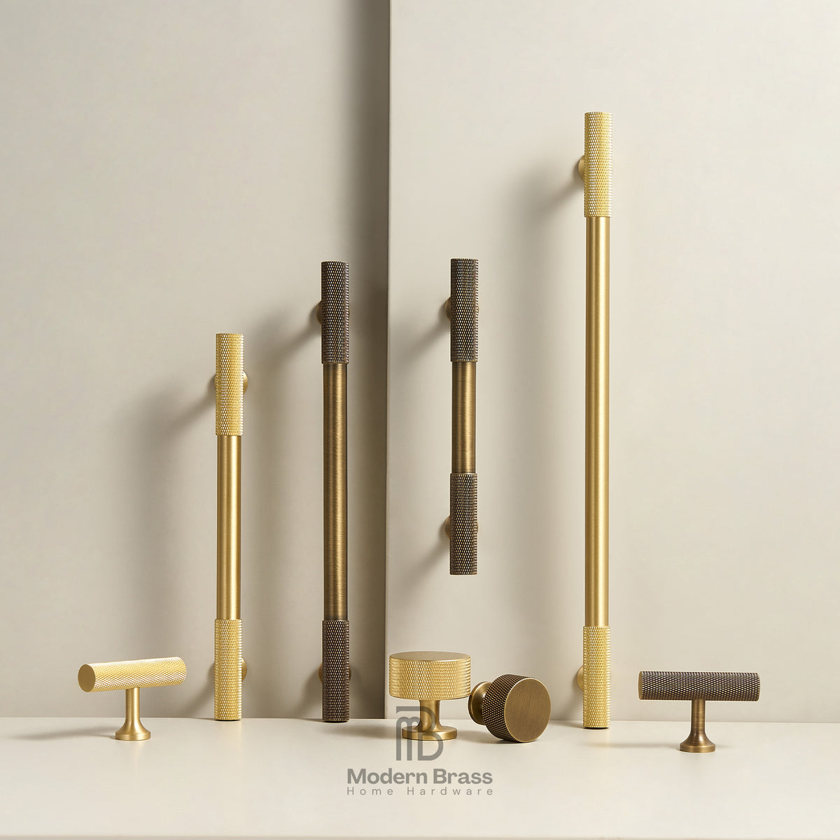 A collection of modern brass and dark bronze cabinet handles in various shapes and sizes, displayed on a white surface against a neutral beige background. The handles feature textured grips and polished finishes.