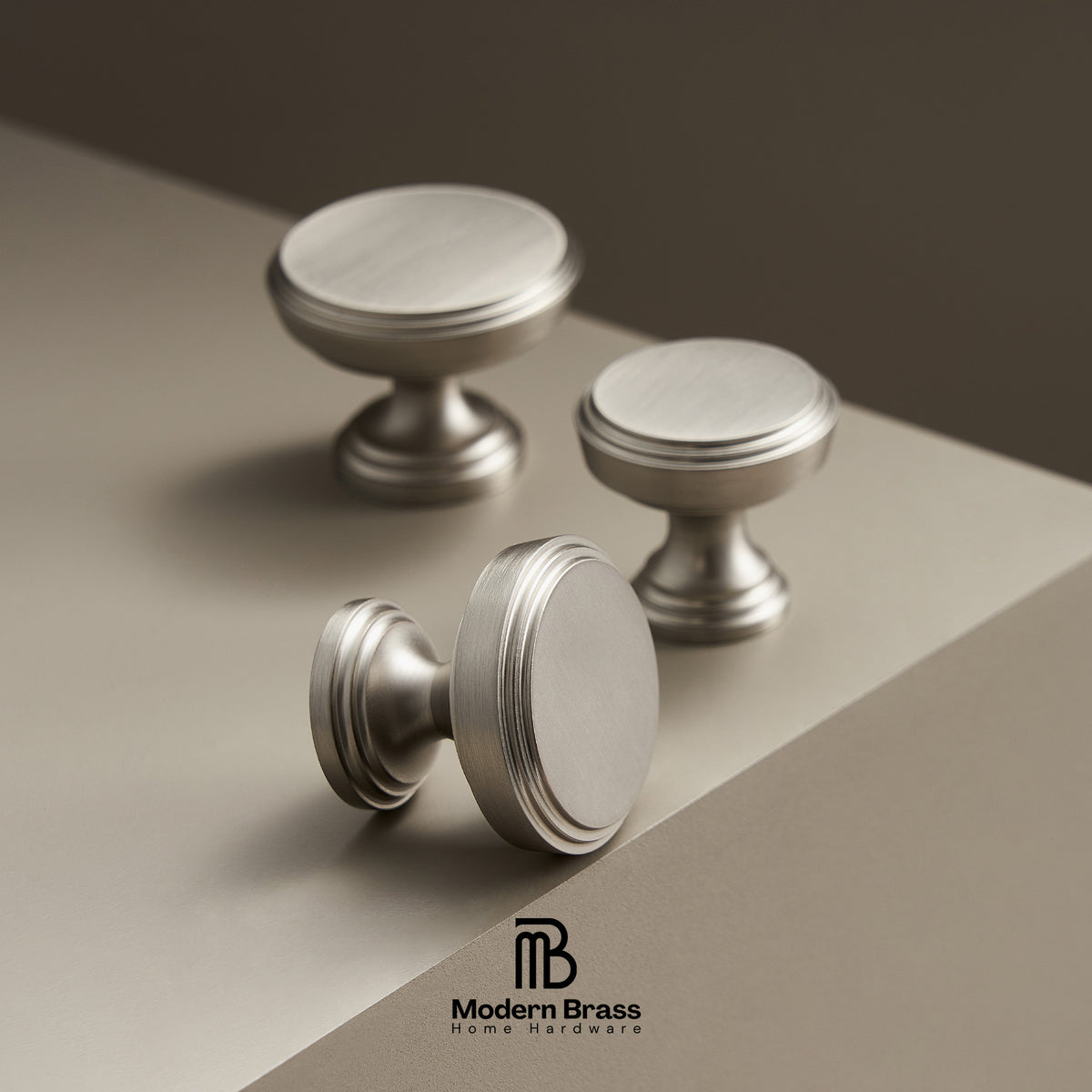 Three metallic cabinet knobs on a gradient background with 'Modern Brass' branding.