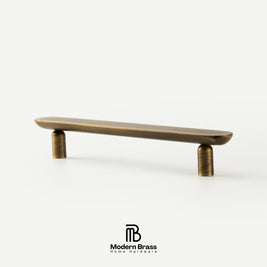 Three round cabinet knobs in black, matte brass, and brushed brass are arranged on a light beige surface against a warm beige background. The Modern Brass logo is visible at the bottom.
