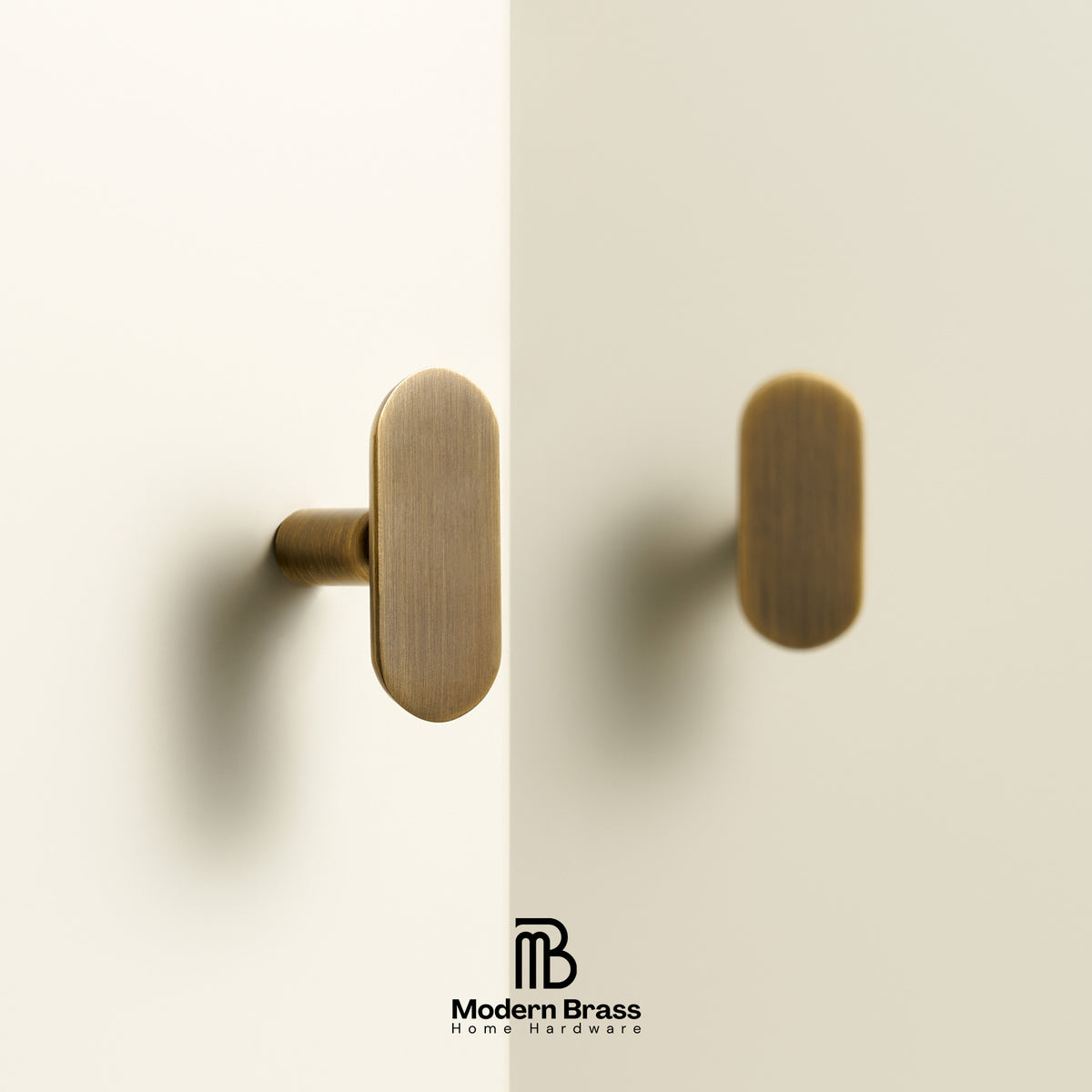 Two oval brass cabinet knobs mounted on a light beige door, with a vertical seam down the center and a Modern Brass logo at the bottom.
