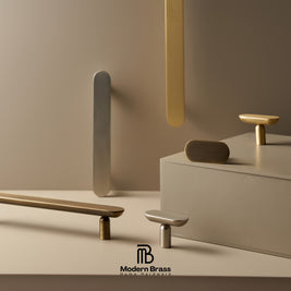 A styled product display of modern brass and silver cabinet knobs and pulls on a minimalist beige background with geometric props. The Modern Brass logo is visible at the bottom.