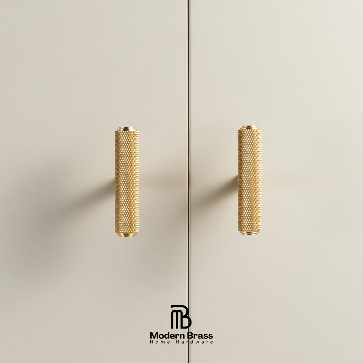 Two modern cylindrical brass cabinet handles with a textured knurled finish, mounted on a light beige wall or door. A vertical seam runs down the center, and the 'Modern Brass' brand logo is visible at the bottom.