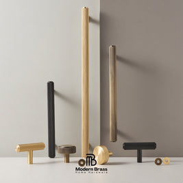 A collection of modern brass and black metal cabinet hardware, including textured vertical bar pulls, T-bar pulls, and round knobs, displayed on a white surface against a split beige and gray background. The Modern Brass logo is visible at the bottom.