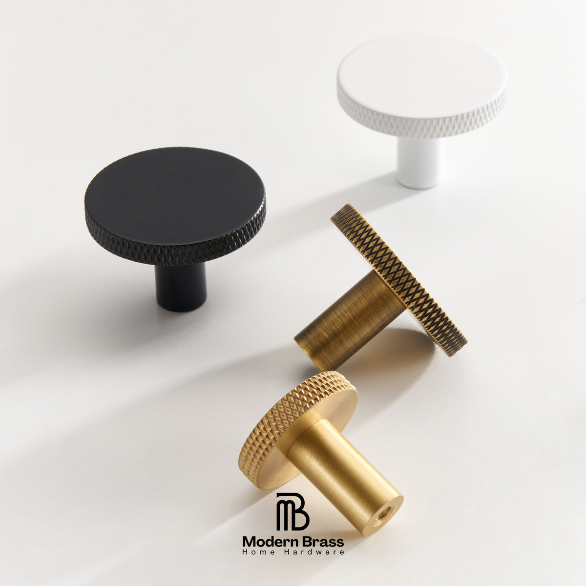 Three round cabinet knobs in black, matte brass, and brushed brass are arranged on a light beige surface against a warm beige background. The Modern Brass logo is visible at the bottom.
