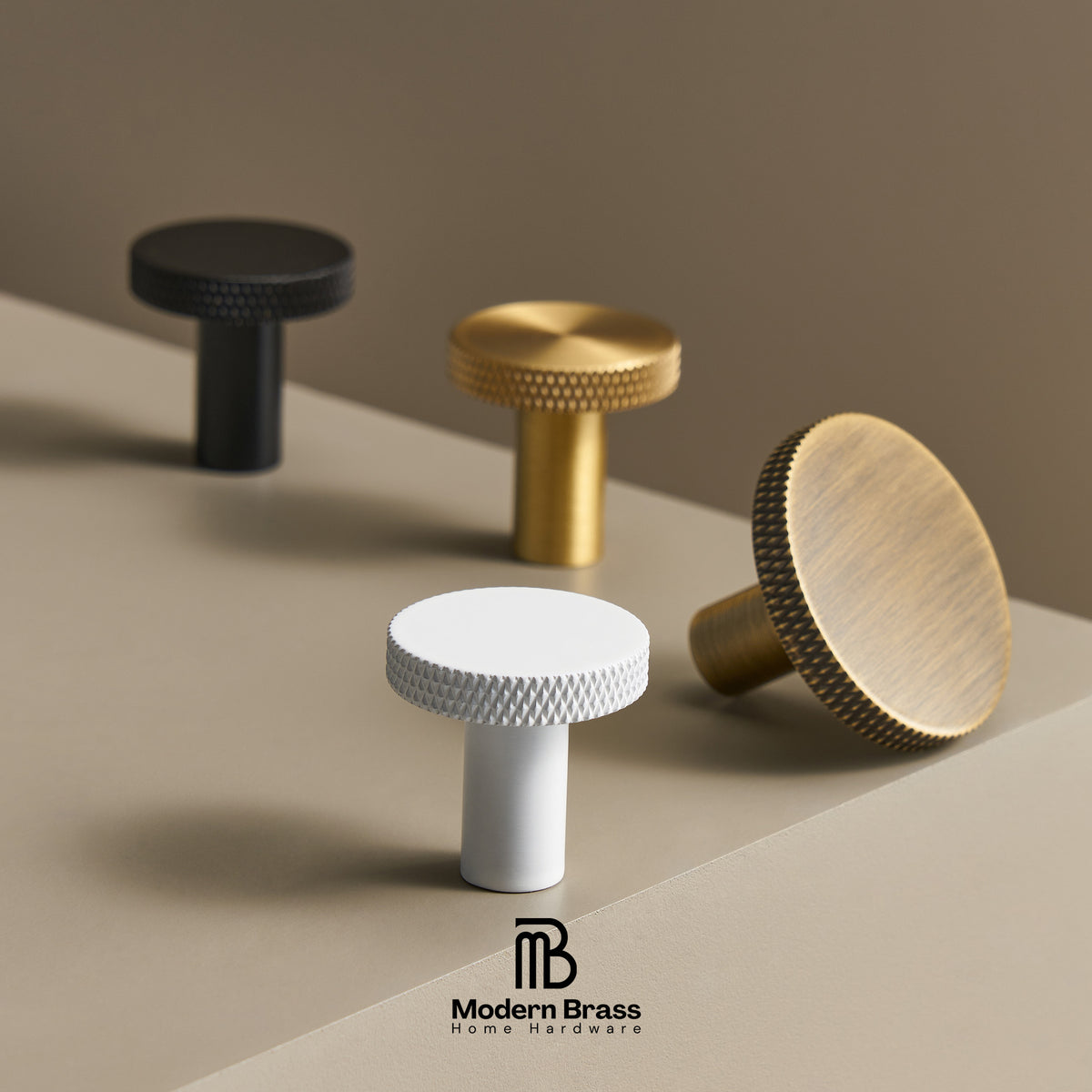 Four modern cylindrical cabinet knobs with knurled edges in black, white, and brushed brass, arranged on a beige surface with a matching background. The Modern Brass logo is visible at the bottom.
