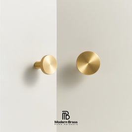 Two round brass wall hooks or knobs in brushed and knurled finishes, mounted on a minimalist off-white wall with a vertical dividing line. The Modern Brass logo is visible at the bottom.