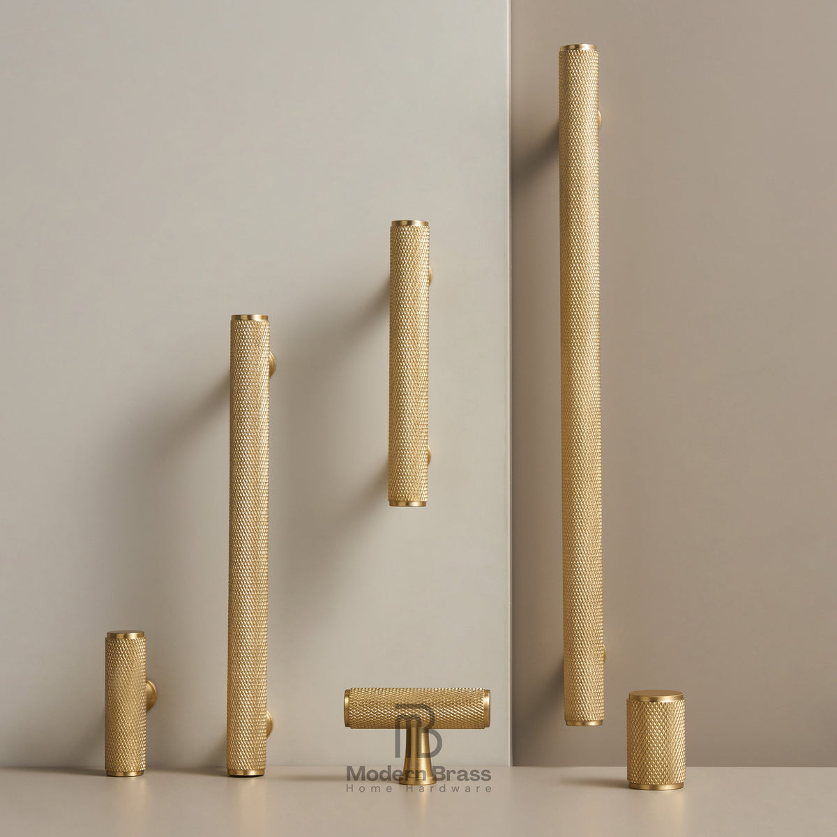 Five brass bathroom cabinet handles in various cylindrical and rectangular shapes, displayed on a light beige surface against a neutral beige background.