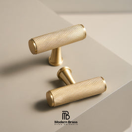 Three round cabinet knobs in black, matte brass, and brushed brass are arranged on a light beige surface against a warm beige background. The Modern Brass logo is visible at the bottom.