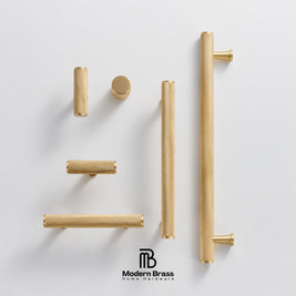 Six brass cabinet handles in various shapes and sizes, including two long vertical bar pulls, two horizontal bar pulls, two short cylindrical pulls, and one round knob, arranged on a light gray background with the Modern Brass logo at the bottom.