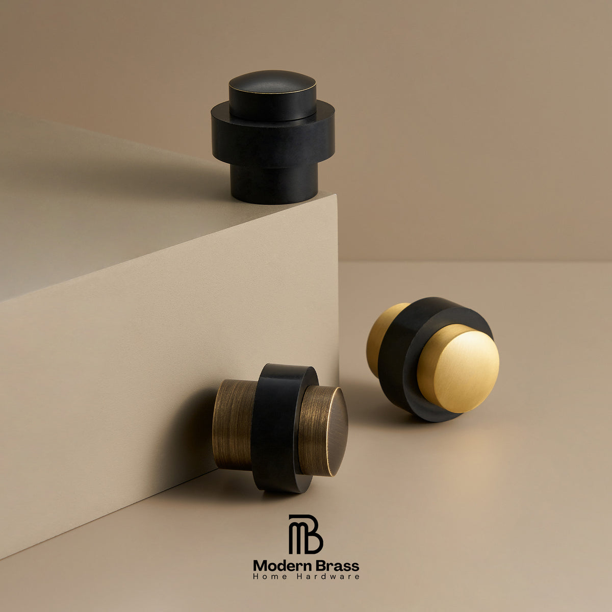 Three modern brass and black home hardware knobs displayed on a beige studio set, with the Modern Brass logo at the bottom.