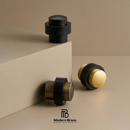 Three modern brass and black home hardware knobs displayed on a beige studio set, with the Modern Brass logo at the bottom.