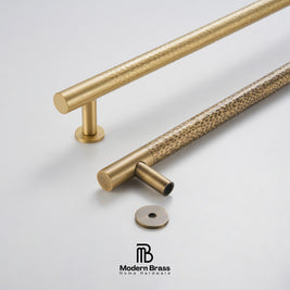 Gold cabinet handles with textured finish on a light gray background, featuring the Modern Brass logo.