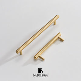 Three round cabinet knobs in black, matte brass, and brushed brass are arranged on a light beige surface against a warm beige background. The Modern Brass logo is visible at the bottom.