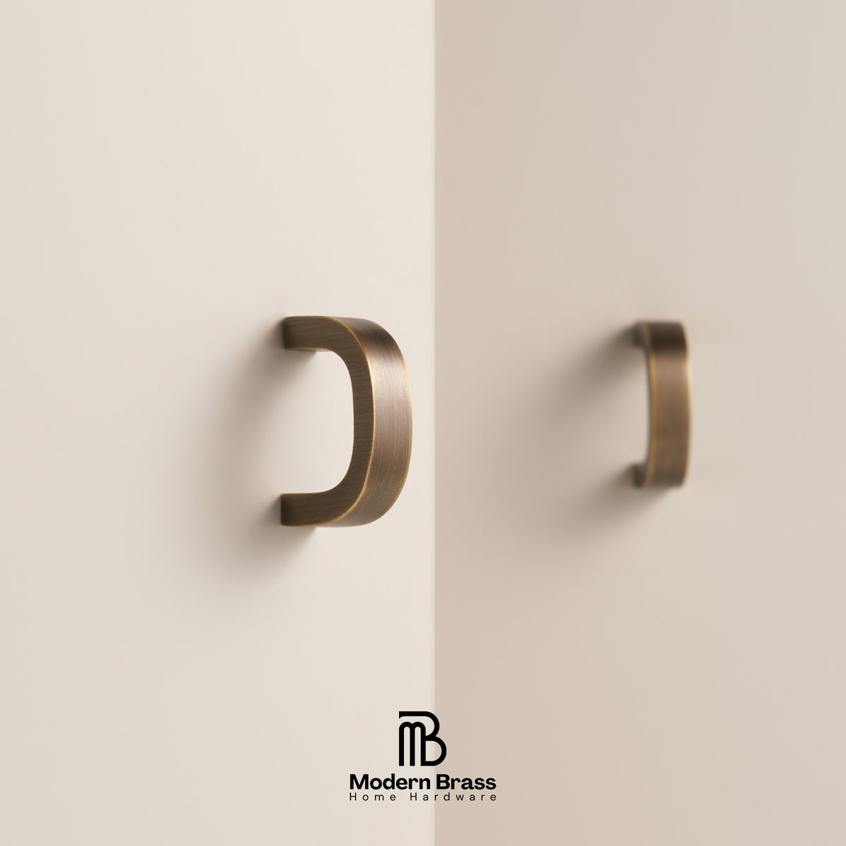 Two modern curved cabinet handles in a brushed brass finish mounted on a minimalist off-white wall, with the Modern Brass Home Hardware logo at the bottom.