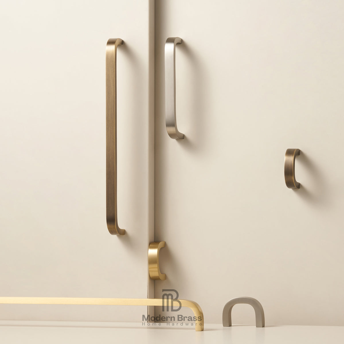 Modern brass and bronze cabinet handles mounted on a light beige wall, including long vertical bar handles, a smaller curved pull, and a top-mounted pull, with a Modern Brass logo at the bottom.
