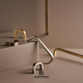 Three round cabinet knobs in black, matte brass, and brushed brass are arranged on a light beige surface against a warm beige background. The Modern Brass logo is visible at the bottom.