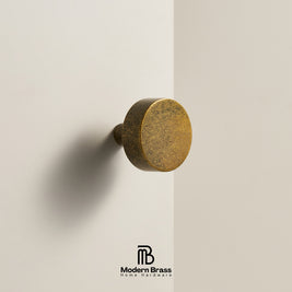 Three round cabinet knobs in black, matte black, and brushed brass are displayed on a light beige surface against a warm beige background. The Modern Brass logo is visible at the bottom.