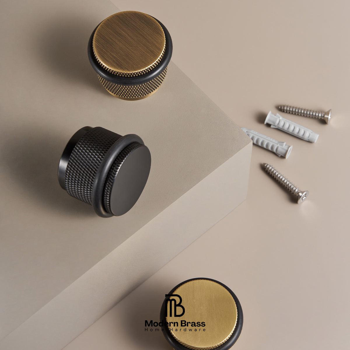 Three round cabinet knobs in brushed brass and matte black finishes, shown with mounting screws and wall anchors on a beige geometric studio background. A Modern Brass logo watermark appears near the bottom.