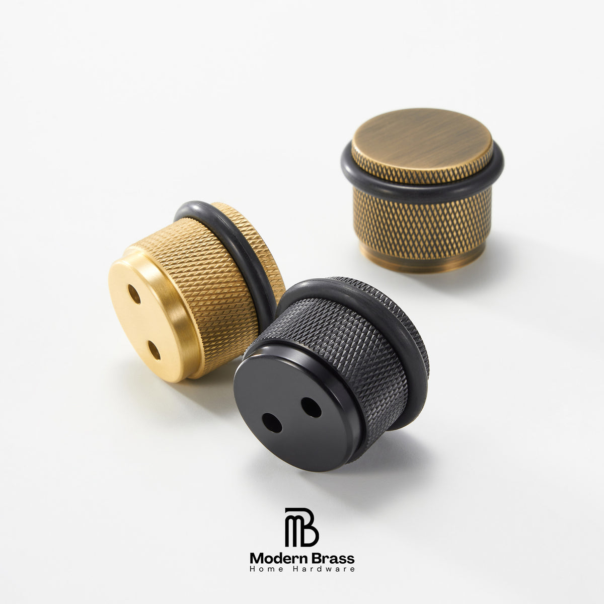 Three brass-toned cylindrical hardware knobs with knurled texture and black rubber grommets, shown on a clean white background. Two are in the foreground and one is slightly behind.