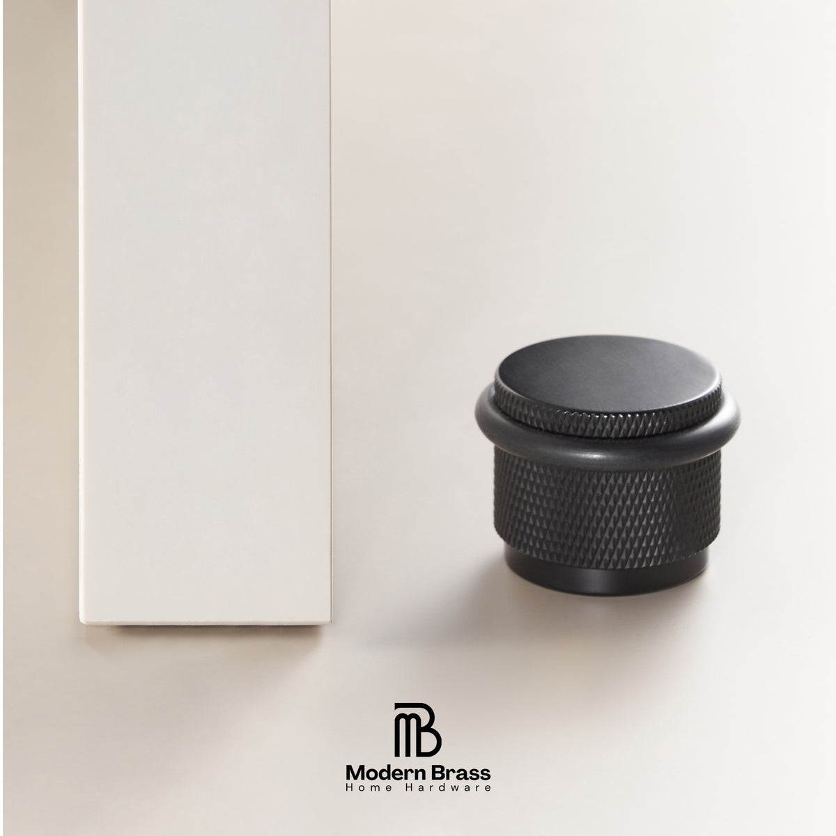 Three round cabinet knobs in black, matte black, and brushed brass are displayed on a light beige surface against a warm beige background. The Modern Brass logo is visible at the bottom.