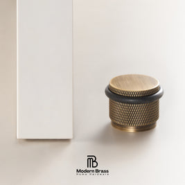 A brass drawer knob with a textured knurled pattern and a brushed gold top, shown next to its white packaging box on a light beige background. The Modern Brass logo is visible at the bottom.