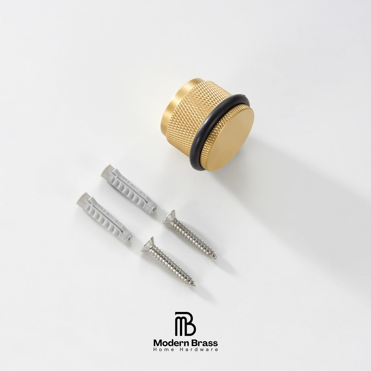 A gold-finished round cabinet knob with a black rubber gasket, shown with two silver wall anchors and two screws on a clean white background. The Modern Brass logo is visible at the bottom.