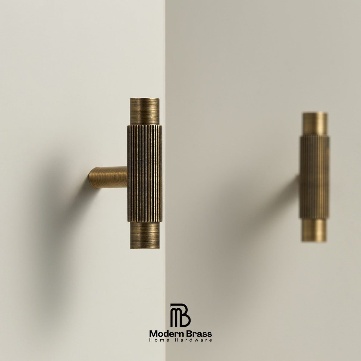 Two brass wall-mounted cabinet knobs with a ribbed cylindrical design, shown on a clean off-white background with one knob in front and one reflected or behind it. The Modern Brass logo appears at the bottom.
