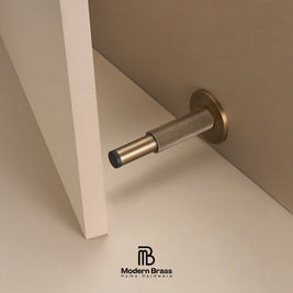 Three round cabinet knobs in black, matte brass, and brushed brass are arranged on a light beige surface against a warm beige background. The Modern Brass logo is visible at the bottom.