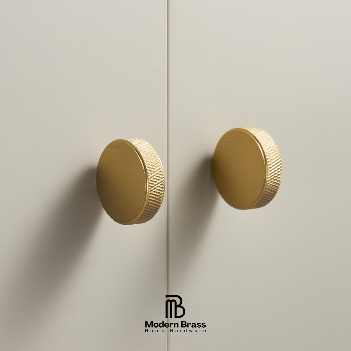 Three round cabinet knobs in black, matte brass, and brushed brass are arranged on a light beige surface against a warm beige background. The Modern Brass logo is visible at the bottom.