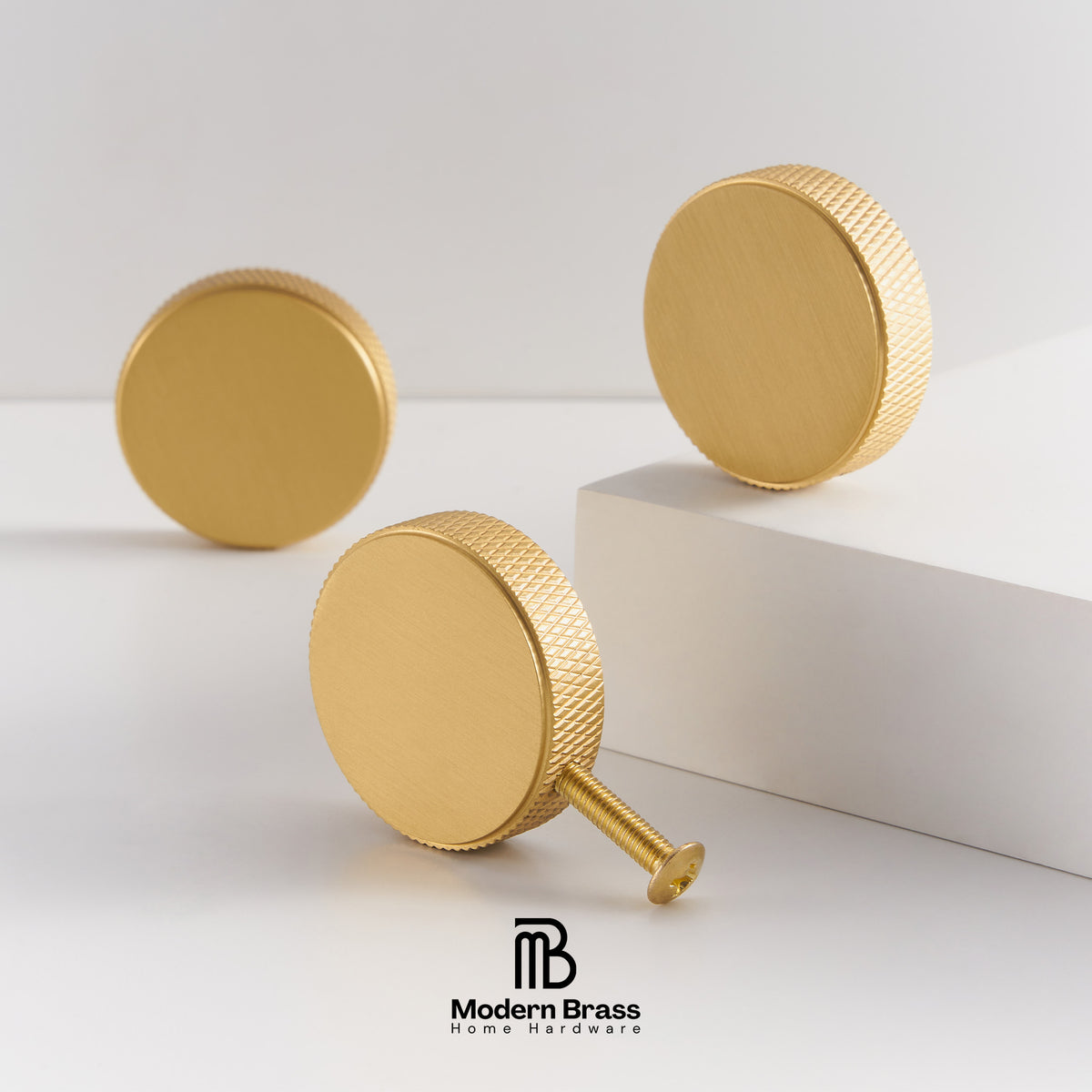 Three gold brass round cabinet knobs with knurled edges, displayed on a clean white studio background with a white block prop. The Modern Brass Home Hardware logo is visible at the bottom.