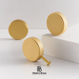 Three gold brass round cabinet knobs with knurled edges, displayed on a clean white studio background with a white block prop. The Modern Brass Home Hardware logo is visible at the bottom.