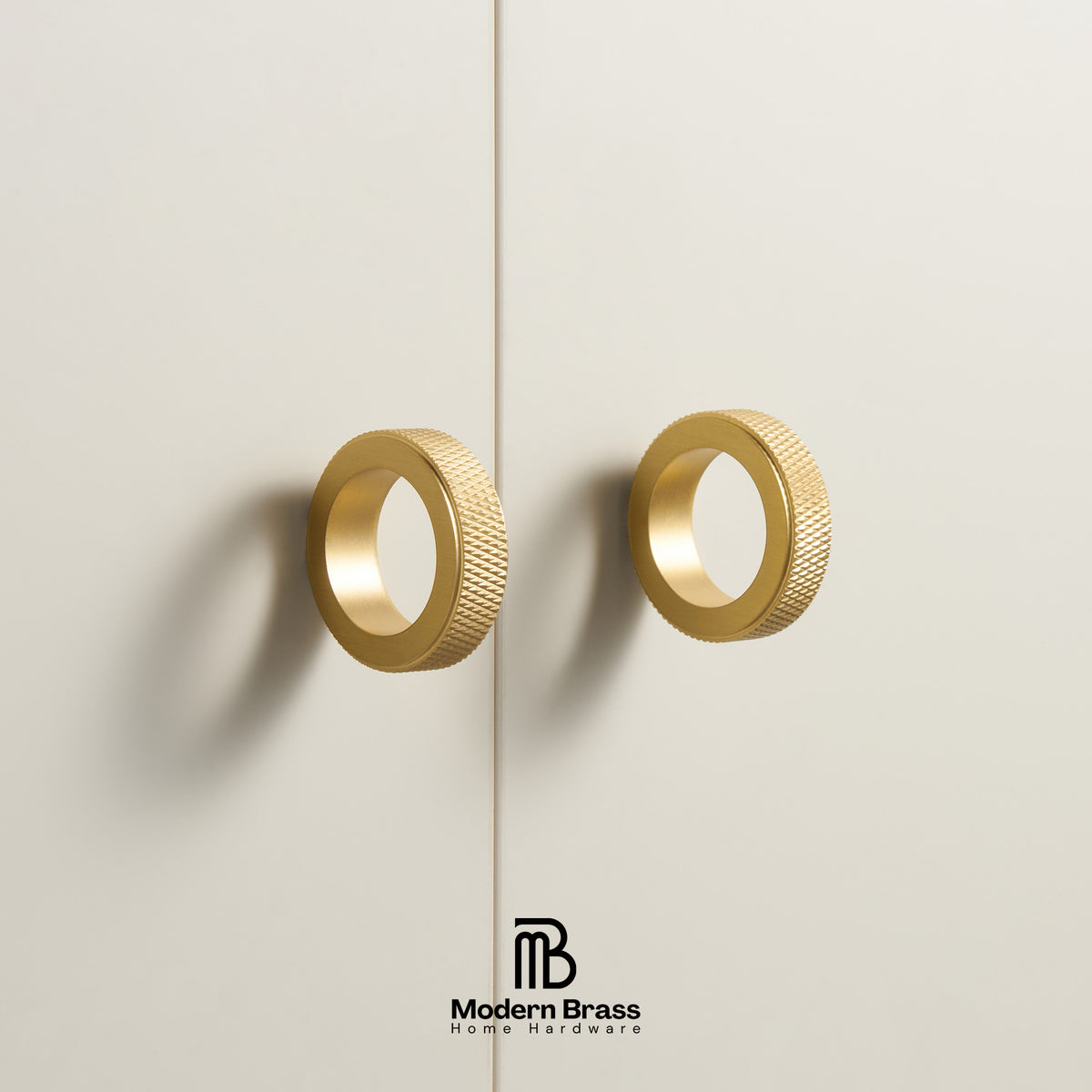 Three round cabinet knobs in black, matte brass, and brushed brass are arranged on a light beige surface against a warm beige background. The Modern Brass logo is visible at the bottom.