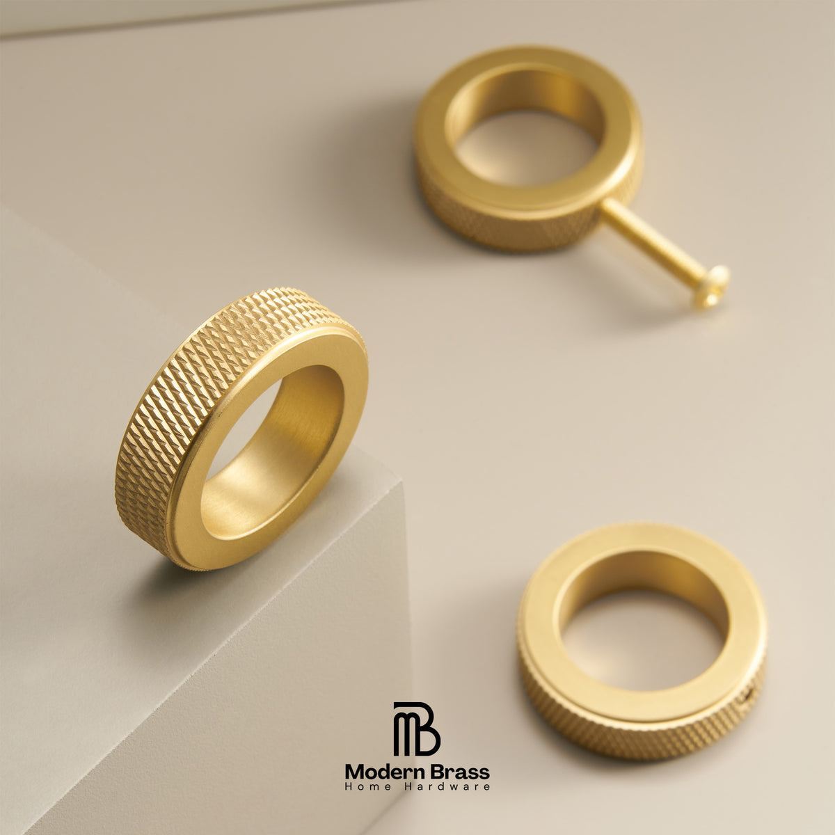 Three gold brass ring components, including a knurled band, a flat ring, and a post with a ball end, arranged on a light beige geometric background. The Modern Brass logo is visible at the bottom.