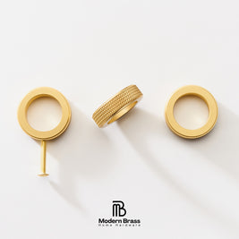 Three gold-finished brass hardware components, including two circular ring-shaped pieces and a textured cylindrical piece with a screw, arranged on a clean white background. The Modern Brass logo is visible at the bottom.