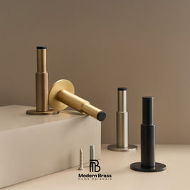 Modern brass hardware set including a round wall plate, mounting bracket, and cylindrical posts in brushed gold, satin silver, and matte black finishes, shown with screws on a beige background. The Modern Brass logo is visible at the bottom.