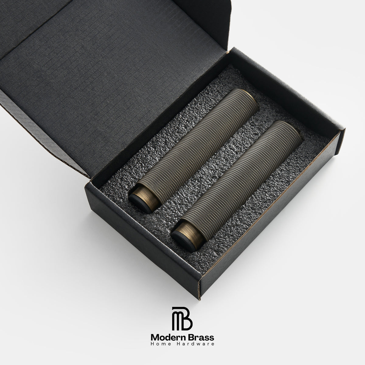 Two dark metallic cylindrical brass instruments, likely mouthpieces or reed cases, presented in a black gift box with foam insert. The Modern Brass logo is visible at the bottom.