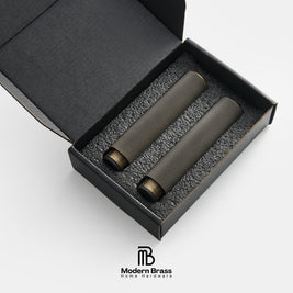 Two dark metallic cylindrical brass instruments, likely mouthpieces or reed cases, presented in a black gift box with foam insert. The Modern Brass logo is visible at the bottom.
