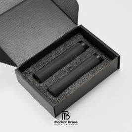 Two black textured cylindrical products displayed inside an open black presentation box with foam insert, on a light gray background. The Modern Brass Home Hardware logo is visible at the bottom.
