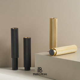 Four brass cylindrical candle holders with textured knurled surfaces in gold and black finishes, arranged on a beige surface with a beige background and a branded Modern Brass block.