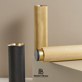 Two cylindrical textured brass home decor pieces, one gold and one dark gray, displayed on a neutral beige background with a Modern Brass logo at the bottom.