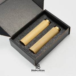 Two brass cylindrical home decor pieces displayed inside an open black presentation box with gray foam insert, on a white background. The Modern Brass logo is visible at the bottom.