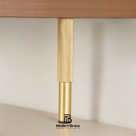 A close-up of a modern brass table leg with a textured knurled upper section and a smooth cylindrical lower section, shown supporting a wooden tabletop against a neutral beige background. The Modern Brass logo is visible at the bottom.