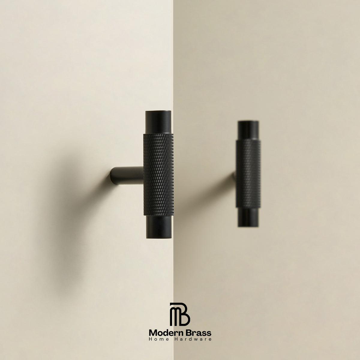 Two modern matte black cabinet handles with knurled textured grips and cylindrical end caps, shown mounted on a split beige wall background. The Modern Brass Home Hardware logo is visible at the bottom.
