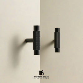Two modern matte black cabinet handles with knurled textured grips and cylindrical end caps, shown mounted on a split beige wall background. The Modern Brass Home Hardware logo is visible at the bottom.