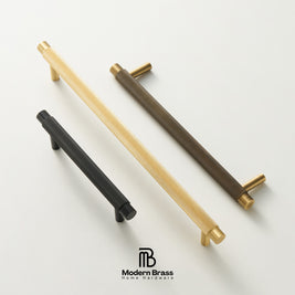 Three modern cylindrical cabinet handles with a ribbed textured finish are displayed diagonally on a clean white background. The handles are shown in three color options: matte black, brushed gold, and dark bronze, each with a polished brass end cap.