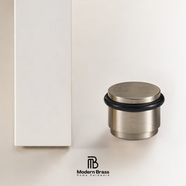 A brushed brass door stopper with a black rubber seal, shown next to its white packaging box on a clean white background, with the Modern Brass logo at the bottom.
