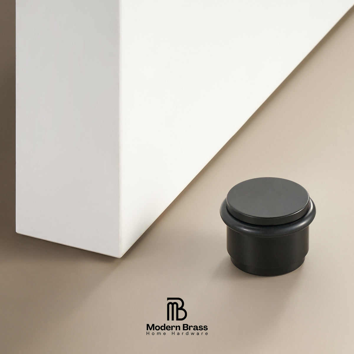 A matte black round cabinet base cap or stopper shown on a beige surface next to a white cabinet corner, with the Modern Brass Home Hardware logo at the bottom.