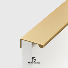 A close-up of a modern L-shaped brass handrail end cap mounted on a white post, with the Modern Brass Home Hardware logo visible at the bottom.